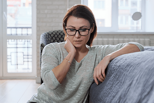 A woman sitting on top of a couch with her hand under the chin.