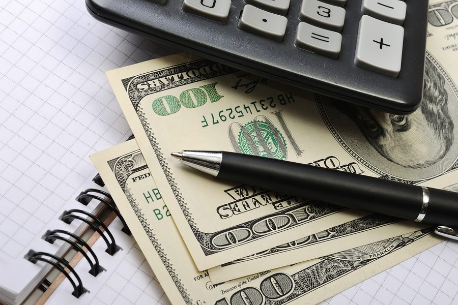 A calculator, pen and money on top of a table.