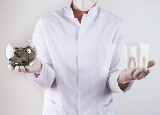 A person in white lab coat holding a cup and a piggy bank.