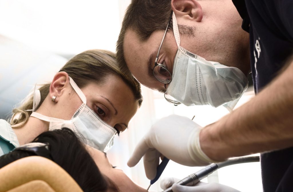 Two people in masks and gloves are working on a patient.