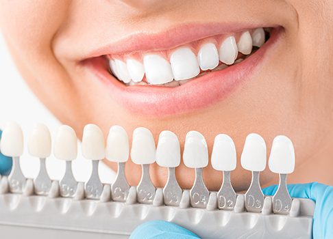 A woman smiles while holding her teeth with dental instruments.