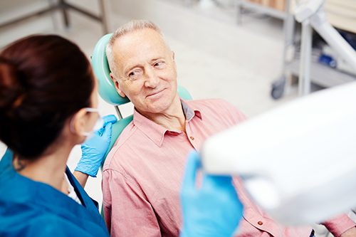 A man sitting in the dentist chair with an assistant.