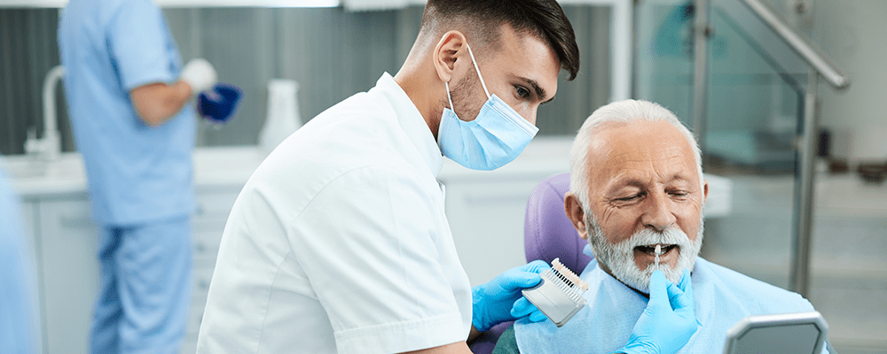 A dentist is examining an older man 's teeth.
