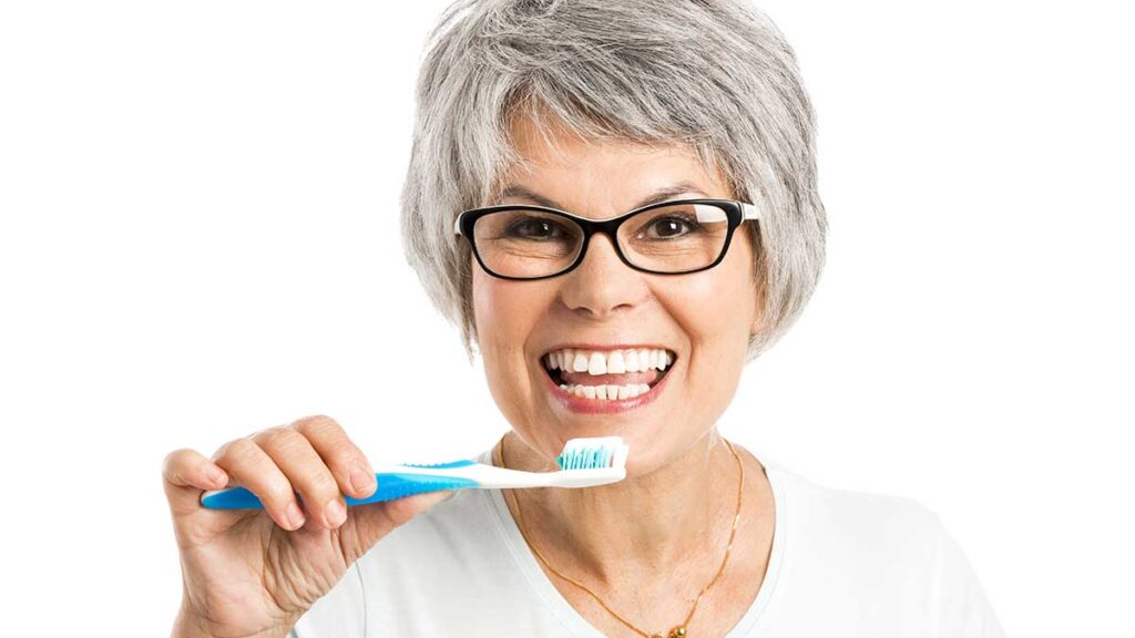 A woman with glasses brushing her teeth.